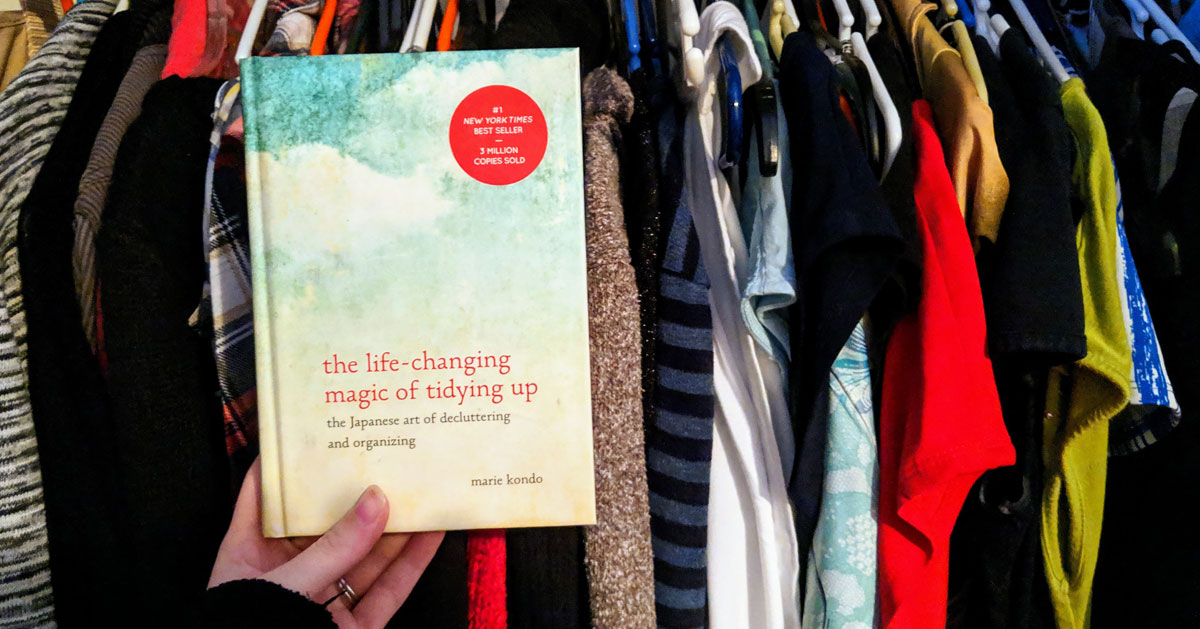 Marie Kondo book held up in front of clothes in closet
