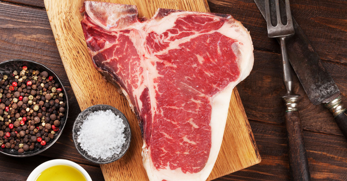 a t-bone steak on cutting board with bowl of salt, etc. nearby